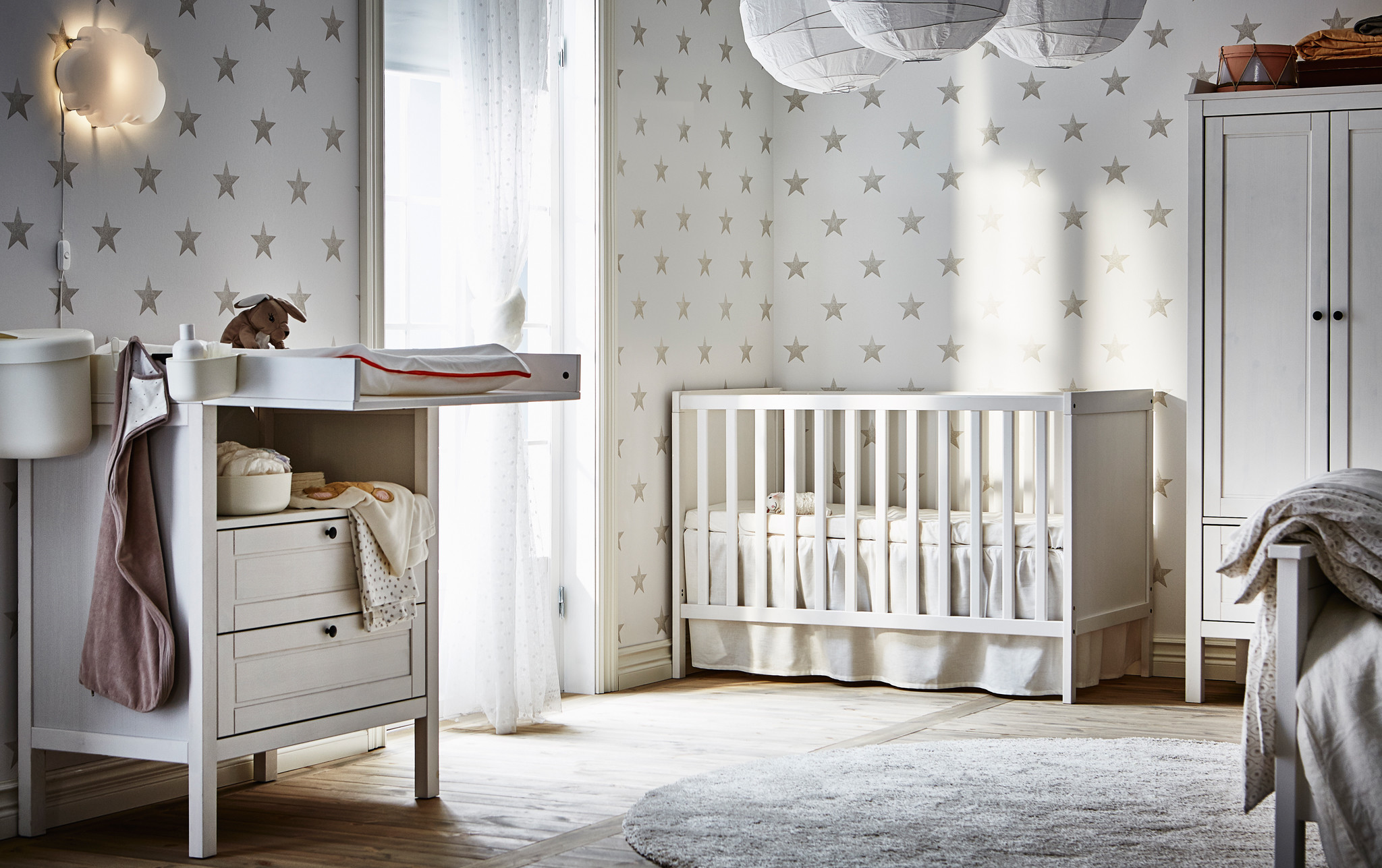 A changing table and cot in a grey and white nursery with star patterned wallpaper