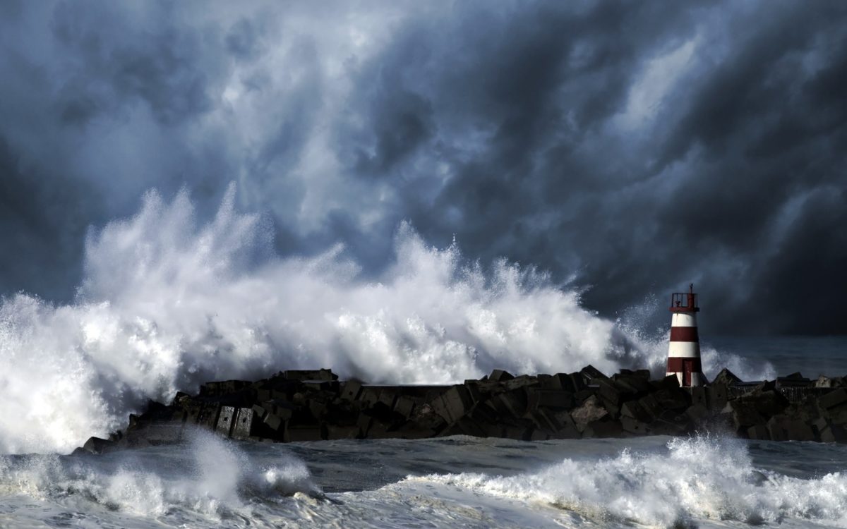Light streaming over a stormy sea from a lighthouse on a rocky shore