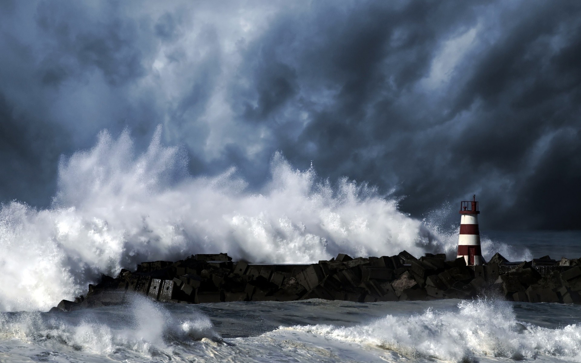 Light streaming over a stormy sea from a lighthouse on a rocky shore. Description from